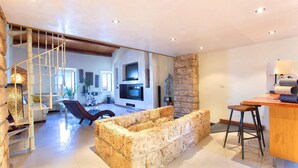 A spacious living area with a stone fireplace, a wooden staircase, and a modern TV setup. - Cavour Loft in Alghero (Alghero)