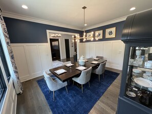 A dining area with a dark wooden table, light grey upholstered chairs, and a blue carpet.