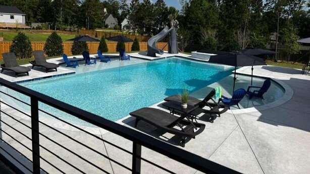 A swimming pool with lounge chairs and a slide, surrounded by a wooden deck and trees. - Golf Rental! House in Champions Retreat (Evans)