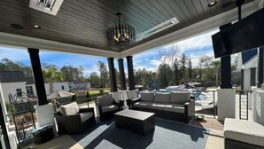 An outdoor patio area with a large sectional sofa, a coffee table, and a TV mounted on the wall. - Golf Rental! House in Champions Retreat (Evans)