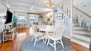 A dining area with a round table, white chairs, and a blue rug. There is a staircase with a fish mural on the wall. - The Dream Location for Your Perfect Vacation  (Branford)