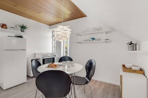 A modern kitchen with a white refrigerator, stove, and black chairs around a white table.