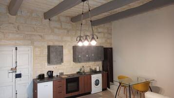Una cocina compacta con lavadora integrada, un comedor con mesa de vidrio y sillas amarillas, y un fondo de pared de piedra.