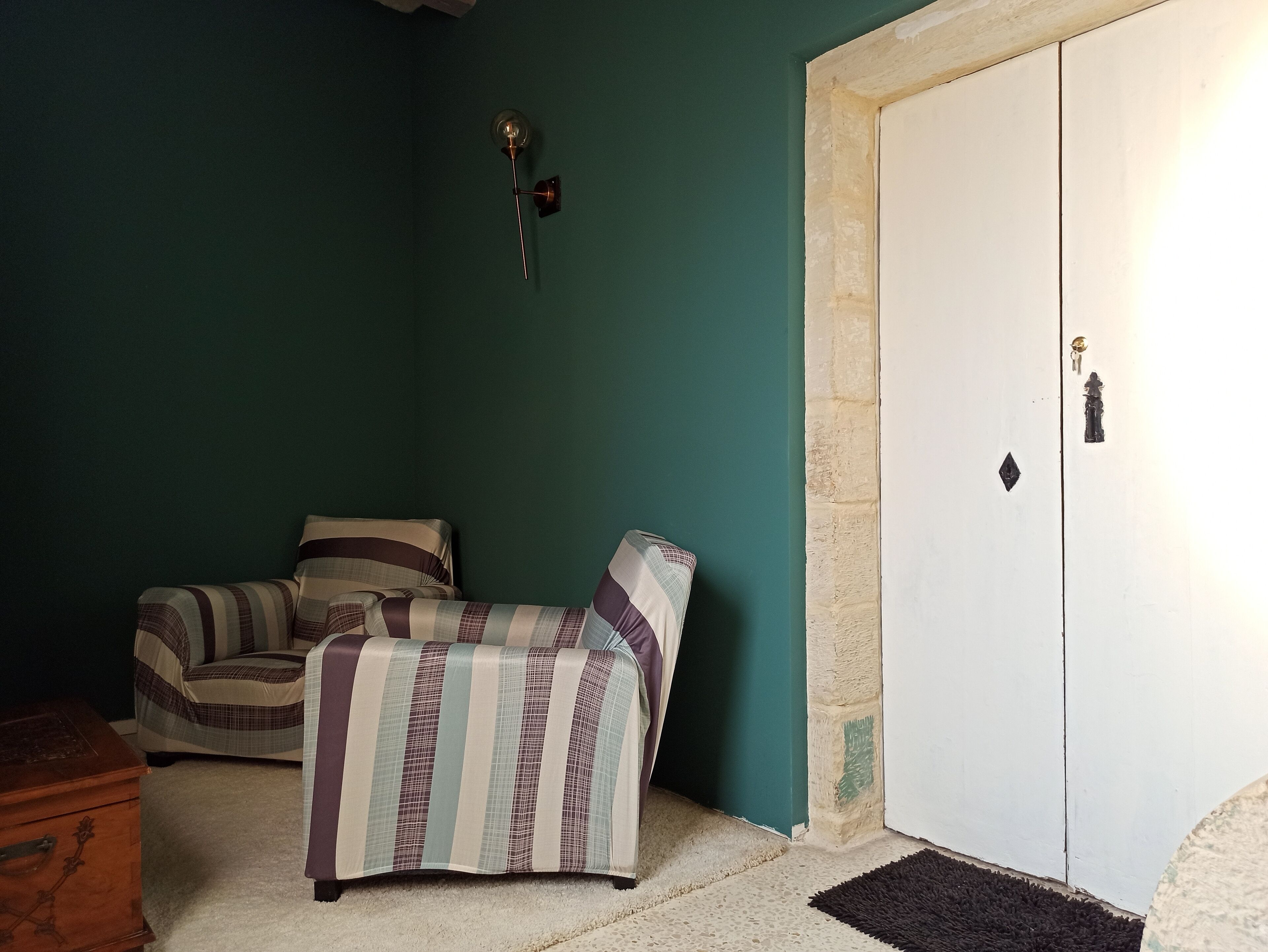 A room with teal walls, a white door, a patterned sofa, and a small wooden chest.