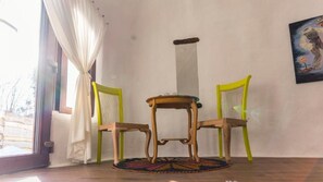 A room with a wooden table and two chairs, a window with curtains, and a painting on the wall. - Pensiunea Dealul Verde (Porumbacu de Jos)
