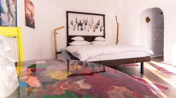 Un dormitorio con cama, cabecera decorada con objetos colgantes, suelo de madera y una obra de arte colorida en la pared.