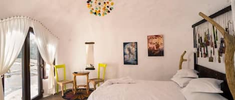 A bedroom with a bed, two chairs, a small table, and a window with curtains.