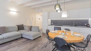 Cozinha moderna com ilha central, mesa de jantar com cadeiras e um sofá cinzento.