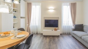 Uma sala de estar moderna com área de jantar, televisão de tela plana na parede e um sofá.