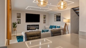 A modern living room with a fireplace, a flat-screen TV, and a dining area with a table and chairs. - Golwg Y M r - Sea View Cottage With Hot Tub (Saundersfoot)