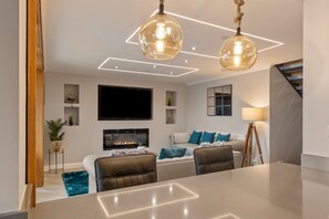 A modern living room with a fireplace, a flat-screen TV, and a dining area with a table and chairs.