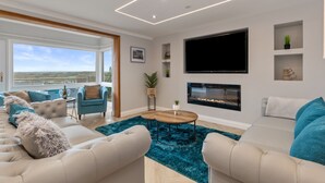 A modern living room with a large TV, a fireplace, and a view of the outdoors. - Golwg Y M r - Sea View Cottage With Hot Tub (Saundersfoot)