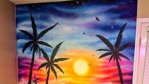 A room with a vibrant sunset mural on the wall, featuring palm trees and a reflective water surface. - The Caribbean Queen Beach House. Beach☆Pools☆Art☆Sleeps 8☆1,000 sq ft. (Panama City)