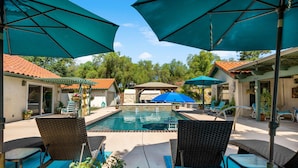 Une piscine entourée de bâtiments aux toits recouverts de tuiles, avec des chaises longues et des parasols à proximité.