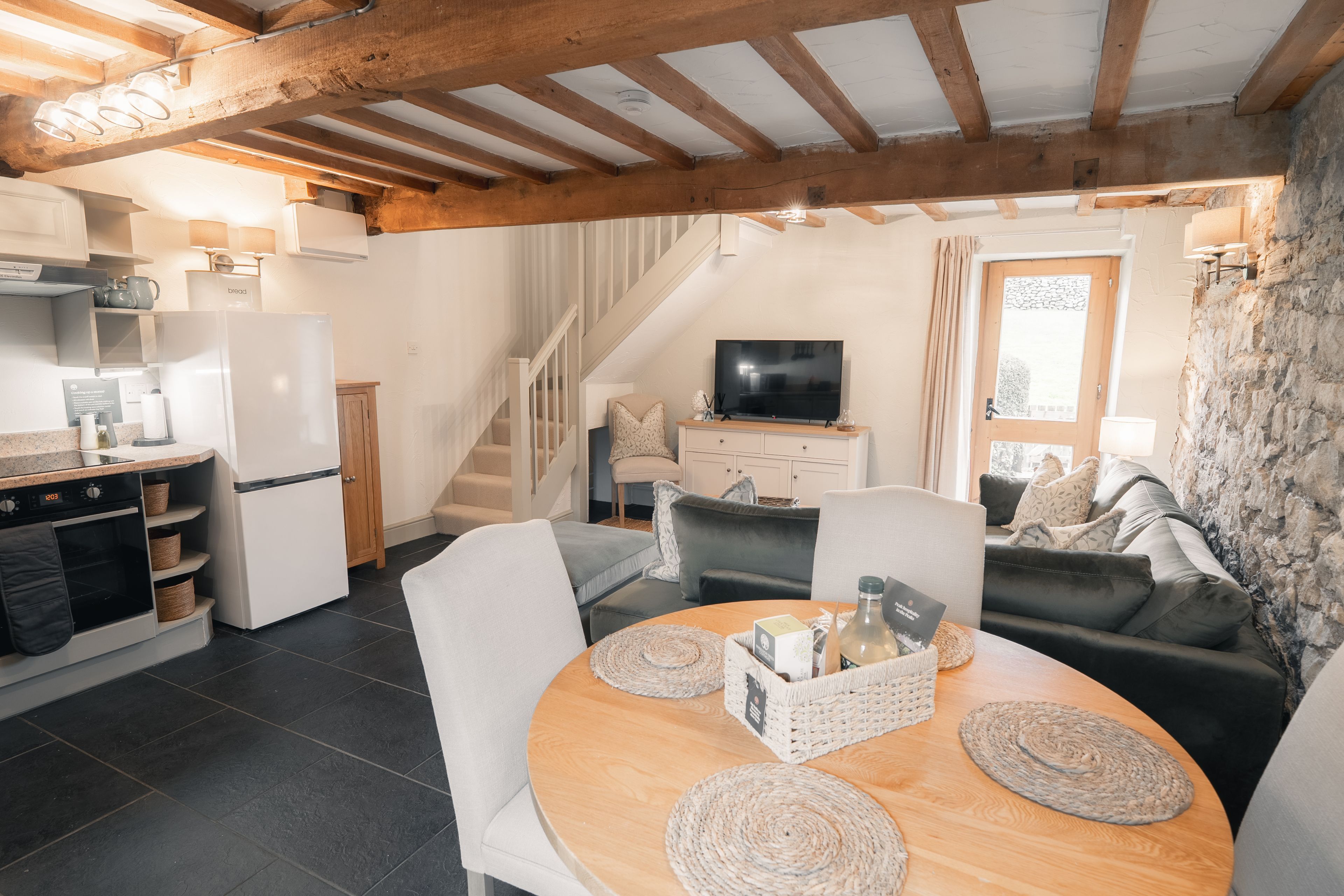 Eine moderne Küche mit Backofen, ein Essbereich mit rundem Tisch und ein Wohnzimmer mit schwarzem Sofa und Fernseher.
