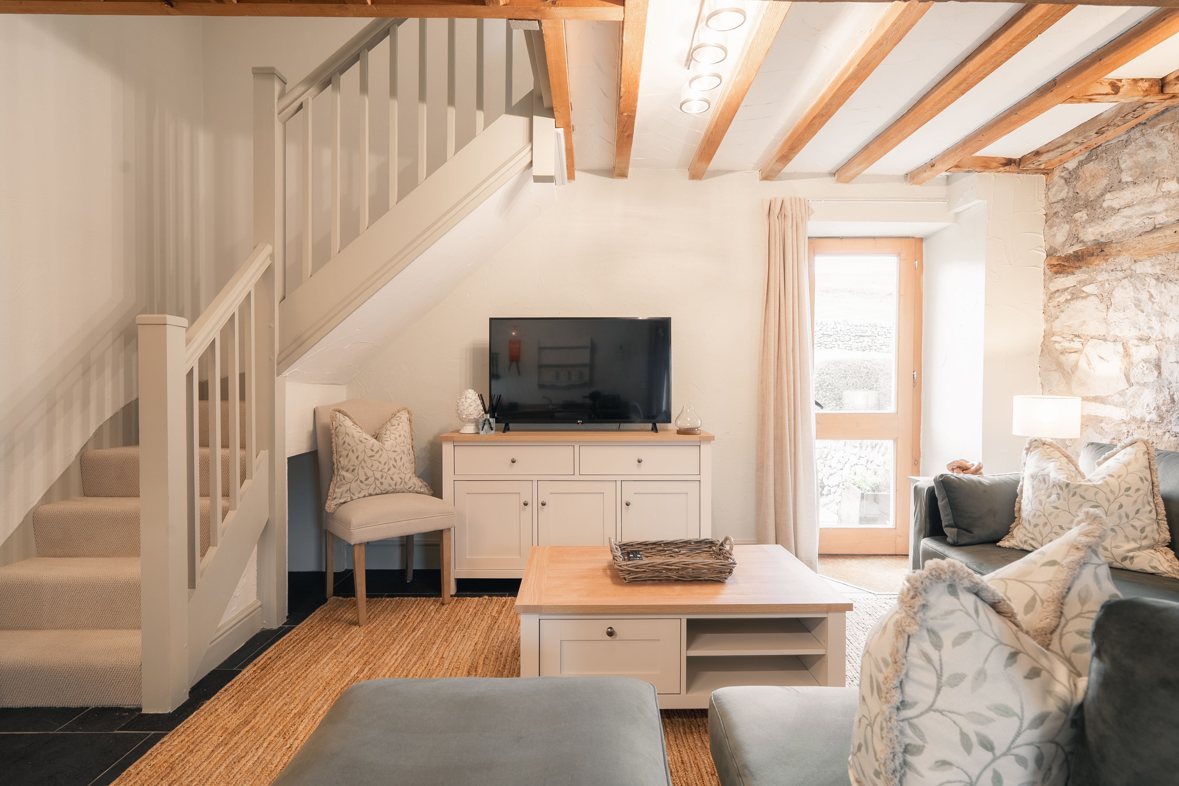 Ein Wohnzimmer mit Treppe, einem Fernseher auf einem Schrank, einem Couchtisch und einem Sofa.
