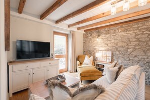 A living room with a television, sofa, and stone wall. - Luxury cottage for three people in the Peak District National Park (Buxton)