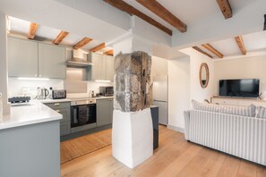 A modern kitchen with white cabinets, a built-in oven, and a microwave. There is a stone pillar in the center of the room. - Luxury cottage for three people in the Peak District National Park (Buxton)
