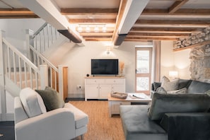 Een woonkamer met een trap, een flatscreen televisie en een stenen muur.