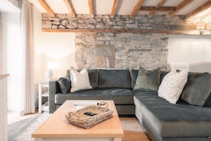 Un salon moderne avec un mur en pierre, un canapé gris aux lignes courbes et une table basse en bois.