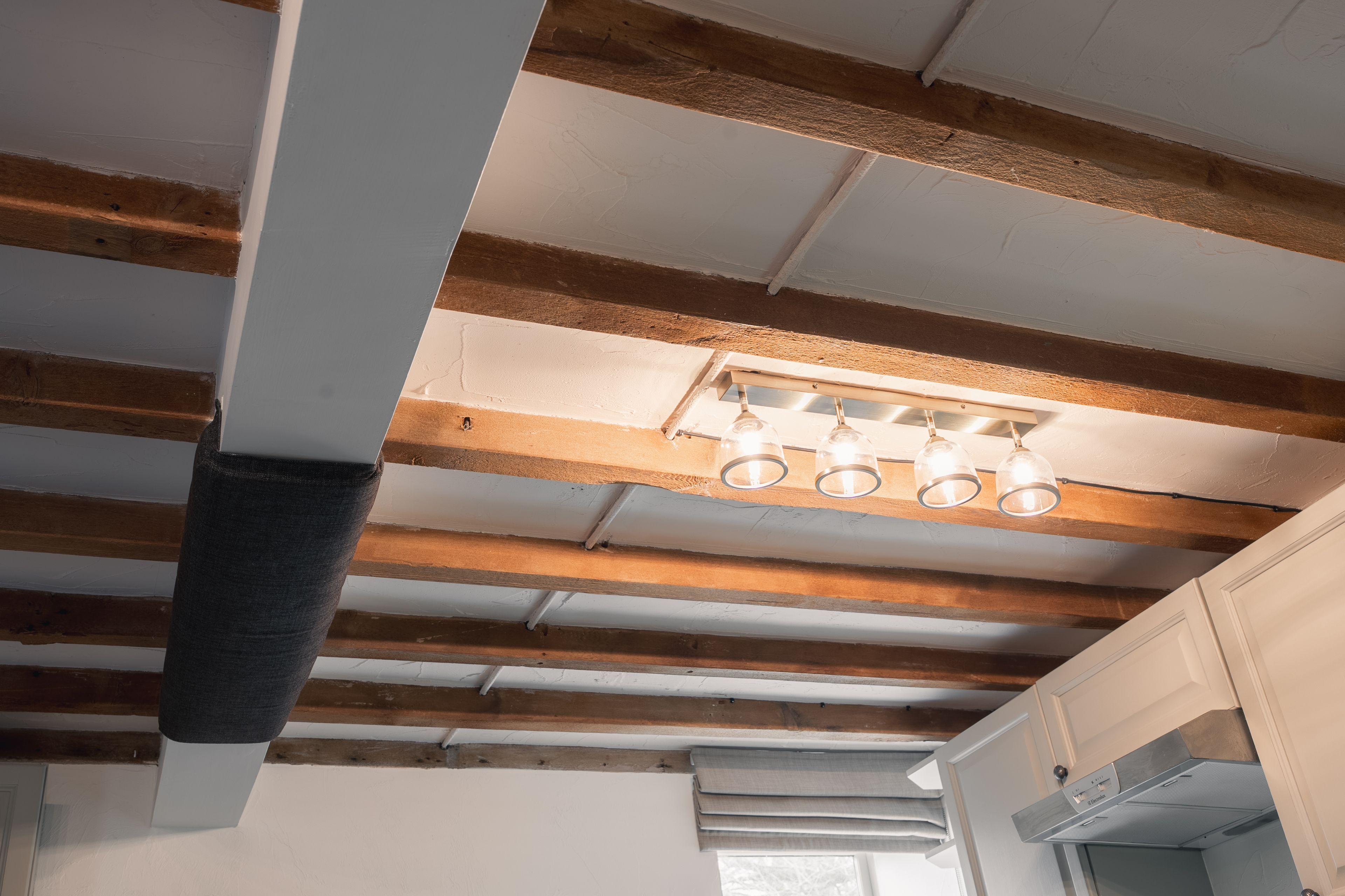 A room with exposed wooden beams, a ceiling light fixture, and a window.