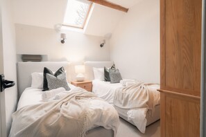 Een slaapkamer met twee bedden, een dakraam en een nachtkastje met een lamp.