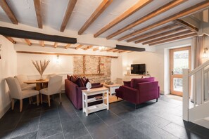 A living room with a stone wall, wooden beams, a TV, and a fireplace. - Country cottage for four people set in 12 acres of Peak District National Park (Buxton)
