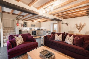Een moderne woonkamer met een rode zithoek, een houten salontafel en een keuken op de achtergrond.