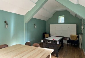 Ein Zimmer mit türkisfarbenen Wänden, einem Holztisch, einem Kicker, einem weißen Schrank und einem Fenster.