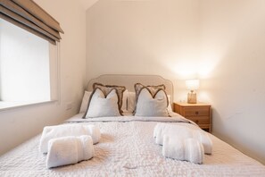 A neatly made bed with a patterned bedspread and two pillows, a bedside lamp, and a nightstand with a lamp.