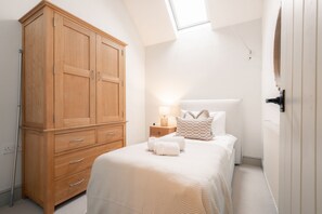 A bedroom with a large wooden wardrobe, a bed with white bedding, and a nightstand with a lamp.
