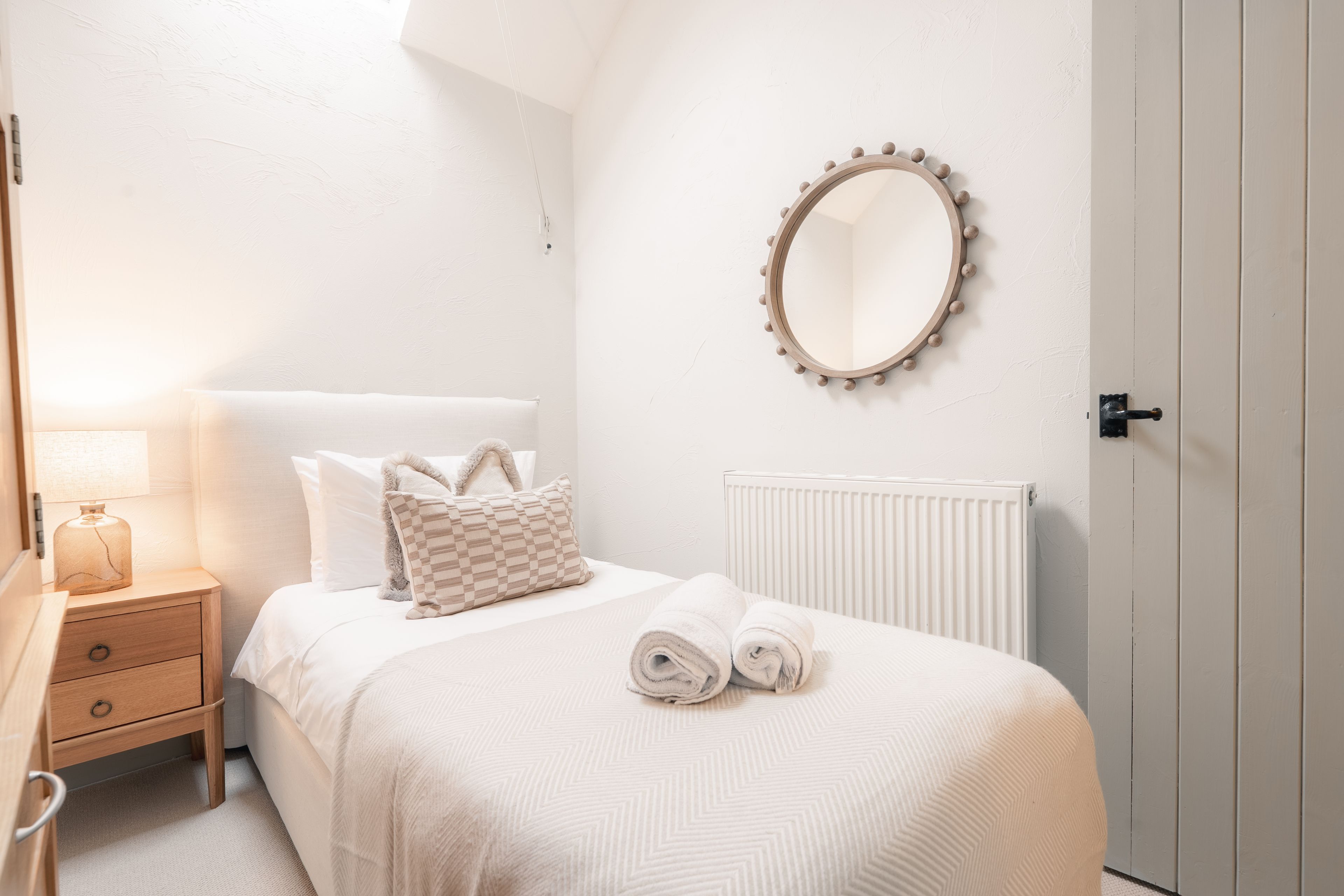 Une chambre à coucher avec un lit, une table de chevet avec une lampe, un radiateur et un miroir fixé au mur.