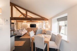 A spacious living area with a dining table, sofas, and a kitchen in the background. - Luxury accessible cottage with two double bedrooms in the Peak District Park (Buxton)