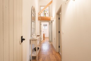 A narrow hallway with wooden flooring, a white door on the left, and a white wall with a window and a light fixture on the right. - Luxury accessible cottage with two double bedrooms in the Peak District Park (Buxton)