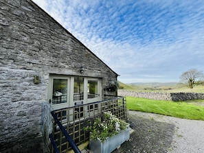Ein Steinhaus mit Balkon, einem Schild mit der Aufschrift 'SHELDON COTTAGE' und Blick auf die Landschaft.