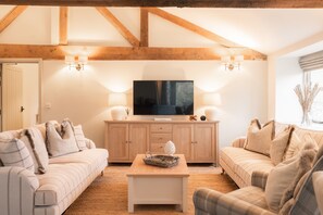 Ein Wohnzimmer mit Fernseher, zwei Sofas, einem Couchtisch und Holzbalken an der Decke.