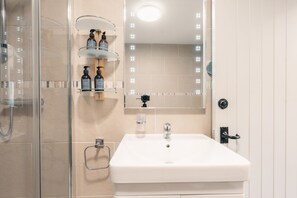 Un baño con cabina de ducha de vidrio, un lavamanos blanco y un espejo con luces.