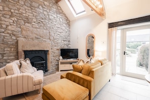 A living room with a stone wall, fireplace, television, sofa, and a large mirror. - Walker's Rest Cottage - perfect for two in the Peaks (Buxton)