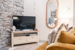 A modern living room with a stone wall, a television on a wooden stand, a mirror with lights, and a cozy sofa.