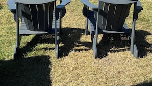 A grassy outdoor area with Adirondack chairs, picnic tables, and a wooden fence. - Studio steps to a private beach!! Ocean views from backyard!! 2 Paddle Boards!!  (Dennis)