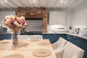 Una cocina moderna con chimenea de ladrillo, muebles blancos y una mesa de comedor con individuales y un jarrón de flores.