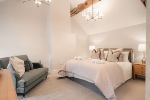 A bedroom with a bed, a sofa, a nightstand, and a chandelier.