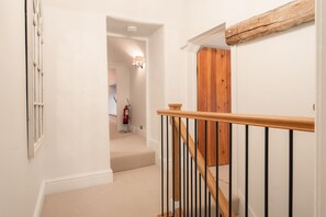 A staircase with a wooden handrail and black balusters, leading to a room with a wooden door and a fire extinguisher on the wall.