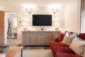 A living room with a flat-screen TV, two wall-mounted lamps, a wooden cabinet, a red sofa, and a patterned rug.