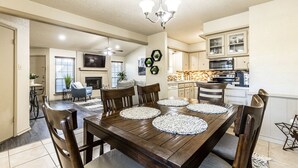 Un comedor con una mesa y sillas de madera, un candelabro y una cocina al fondo.