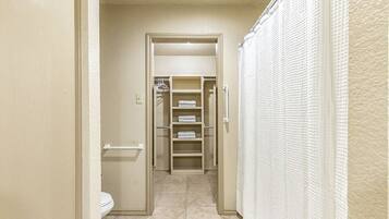En smal gang der fører til et badeværelse med toilet, håndklædestang og bruseforhæng.