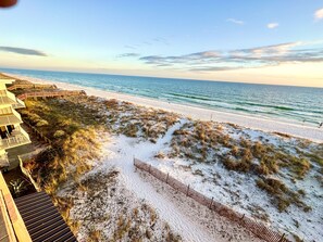 Ein Strand mit einer Holzpromenade, die zu einem Gebäude mit Balkonen mit Blick auf den Ozean führt.