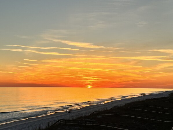 A sunset over a beach with a wooden boardwalk.