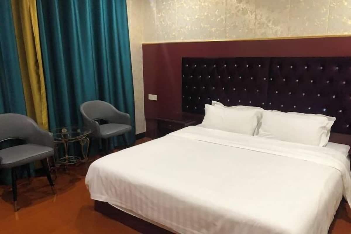A hotel room with a large bed, two chairs, a small table, and a decorative wall panel.