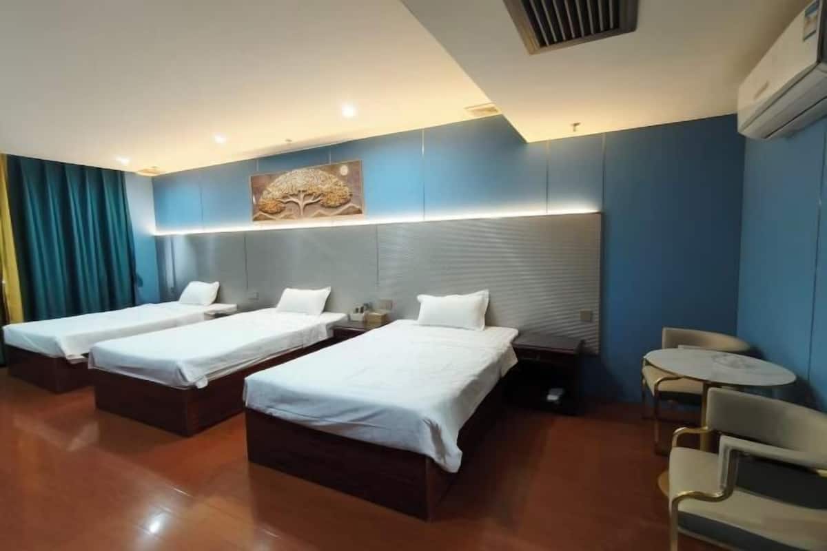 A hotel room with three single beds, a small table, a chair, and a wall-mounted artwork.
